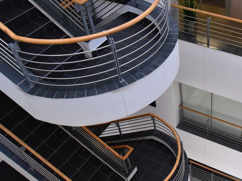 A modern commercial atrium featuring a striking curved staircase with tiled treads, metal balustrades, and wooden handrails.