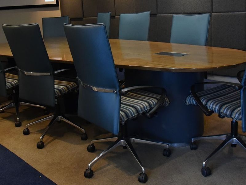 A professional boardroom featuring a large oval meeting table with integrated cable management and acoustic wall paneling for sound control.