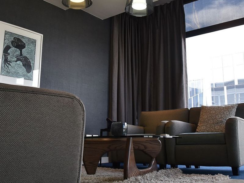 A modern, well-appointed living area featuring dark textured walls, large windows with floor-to-ceiling curtains, and contemporary recessed lighting.