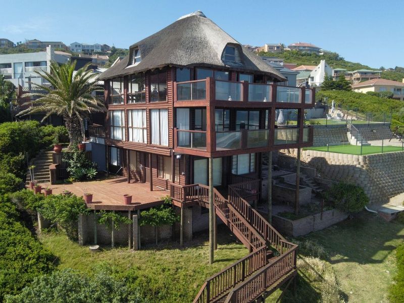 Aerial view of a multi-level timber-clad residence featuring a traditional thatch roof, expansive wrap-around balconies, and tiered outdoor decking.