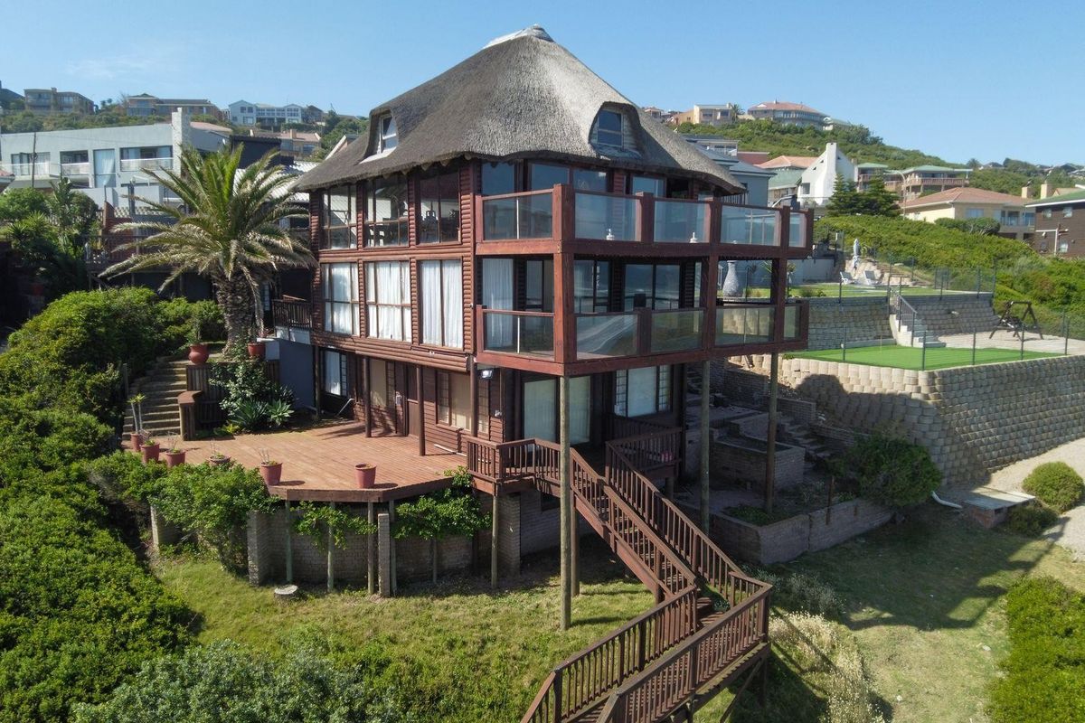 Aerial view of a multi-level timber-clad residence featuring a traditional thatch roof, expansive wrap-around balconies, and tiered outdoor decking.