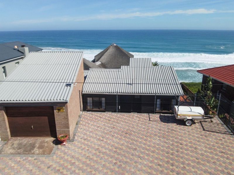 Aerial view of the property featuring a paved driveway, garage, and corrugated metal roofing, situated in a prime coastal location with ocean views.