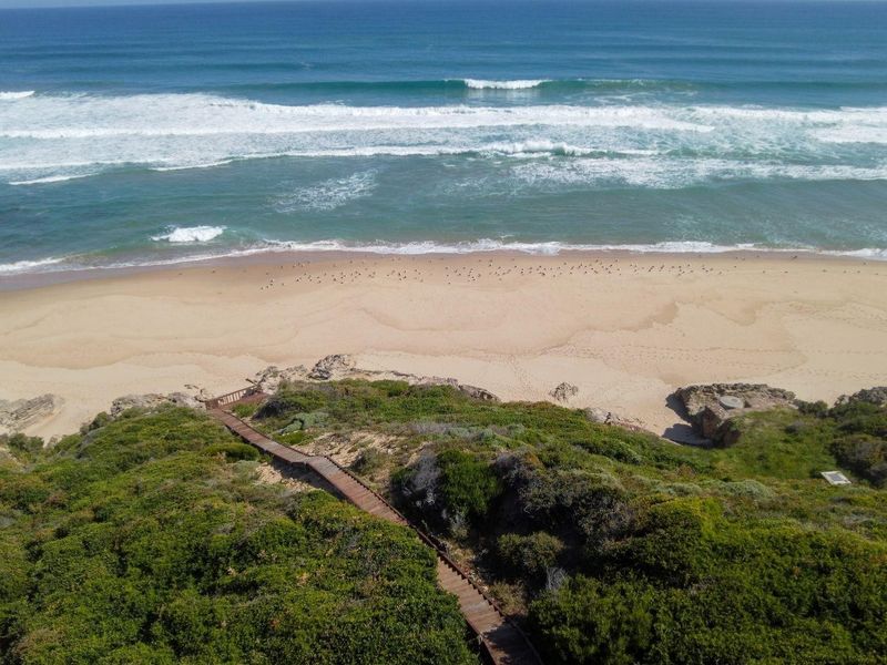 Aerial view of a coastal property featuring a private wooden boardwalk leading down to the sandy beach and ocean.