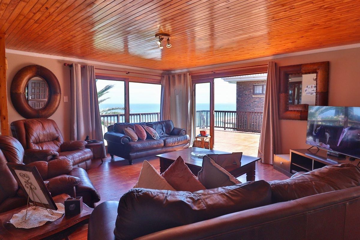 Spacious living room featuring a warm timber tongue and groove ceiling, hardwood flooring, and large sliding glass doors opening onto an outdoor deck with views.