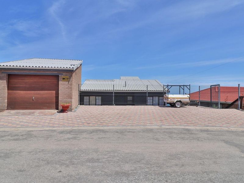 Front view of the property featuring a brick garage, paved driveway, and secure perimeter fencing under a clear sky.