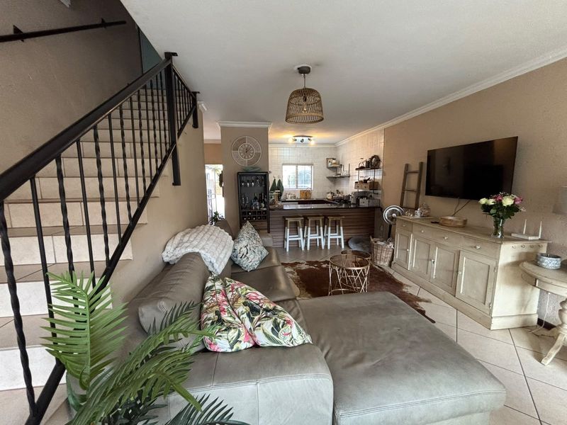 Open plan living area featuring a staircase with metal railing, tiled flooring, and a kitchen with a breakfast bar and built-in cabinetry.