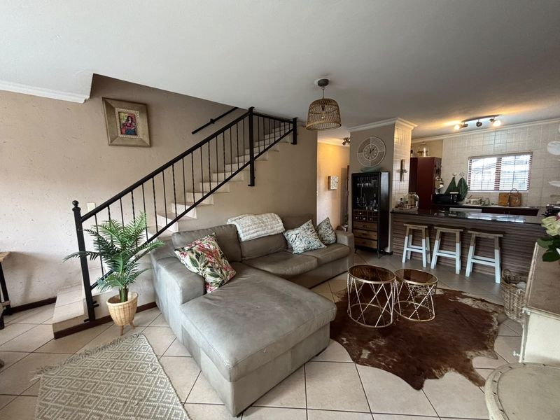 Open-plan living area featuring a staircase with metal balustrade, tiled flooring, and a kitchen breakfast bar, creating a functional and connected living space.