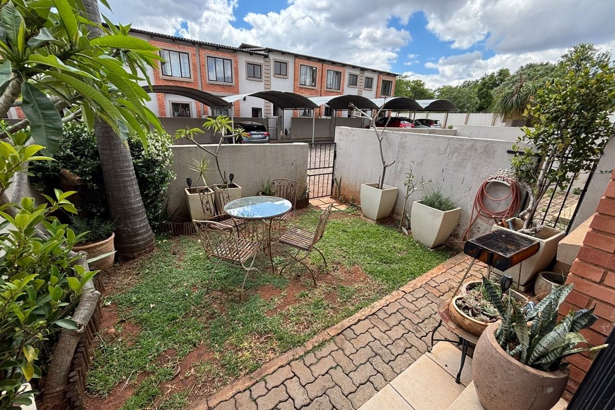 A private rear garden featuring a paved patio area, small lawn, and boundary wall, providing a functional outdoor space for the townhouse.