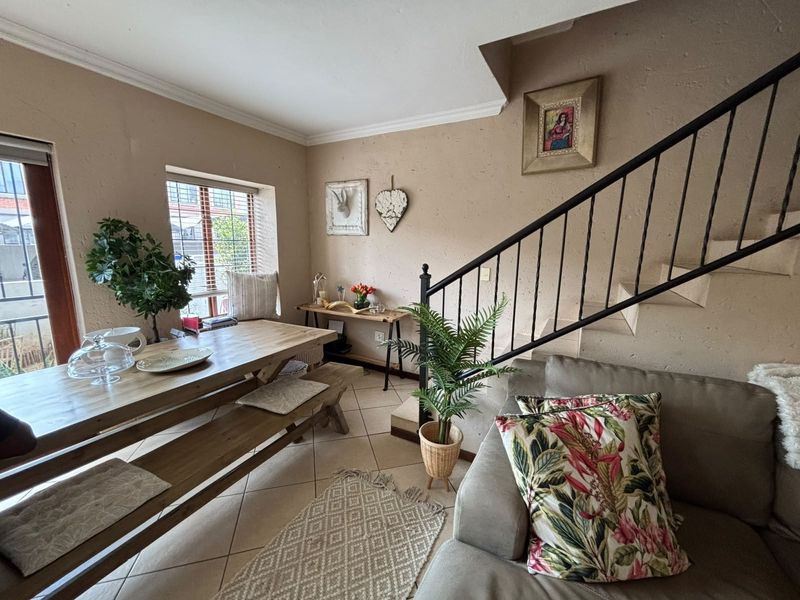 Open plan living and dining area featuring tiled flooring, a staircase with a metal railing, and natural light from the window.