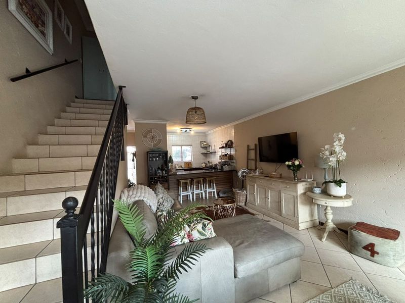 Open-plan living area featuring a tiled staircase with wrought iron balustrade, flowing into a functional kitchen with a breakfast bar and tiled backsplash.