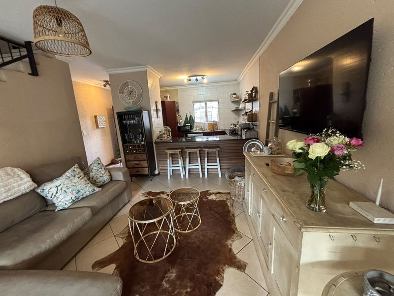 Open-plan living area featuring a kitchen with a breakfast bar, tiled flooring, and a staircase, creating a functional and connected living space.