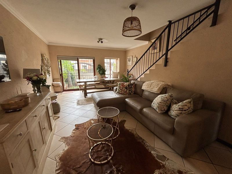 Open-plan living and dining area featuring tiled floors, a staircase with a metal balustrade, and sliding glass doors leading to the outdoor space.