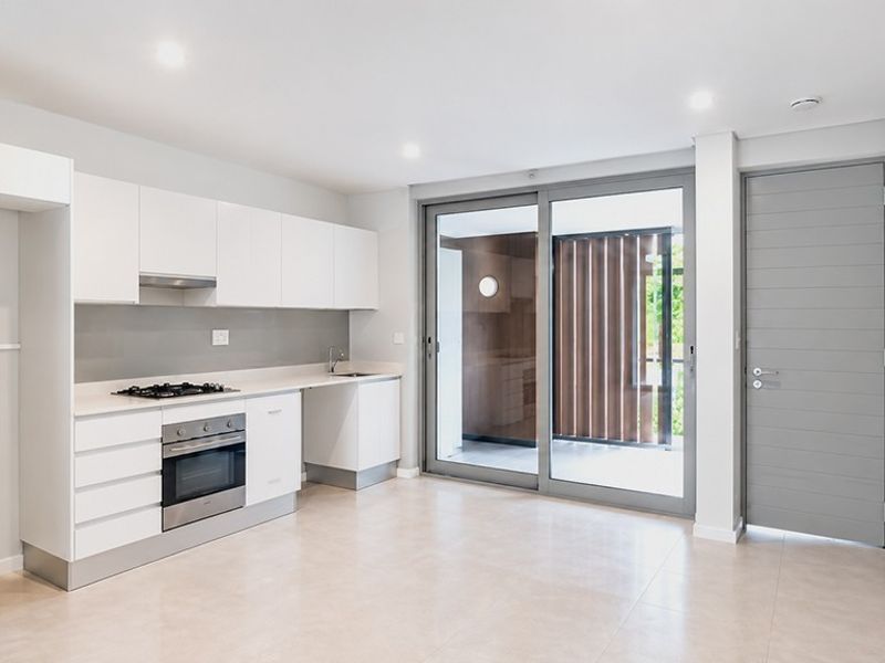 Modern open-plan kitchen featuring sleek white cabinetry, integrated appliances, and large sliding doors leading to a private balcony area.