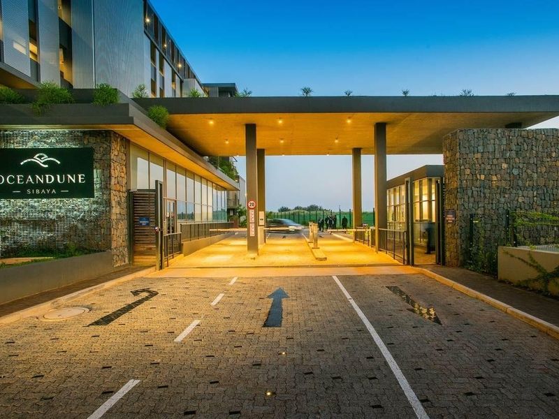 Modern security entrance and gatehouse for Oceandune Sibaya, featuring stone cladding, paved driveway, and integrated lighting.