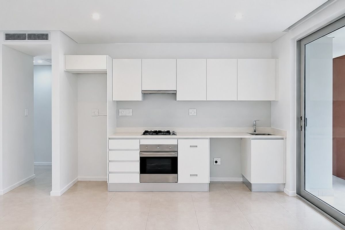 Modern, minimalist kitchen featuring white cabinetry, integrated stainless steel appliances, gas hob, and direct access to an outdoor balcony area.