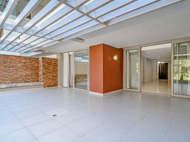 A spacious, modern covered patio featuring a slatted pergola, exposed brick wall, and large sliding glass doors leading into the apartment interior.