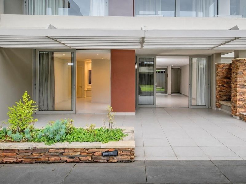 A modern covered patio featuring tiled flooring, a stone-clad planter box, and large sliding glass doors providing seamless access to the interior living space.
