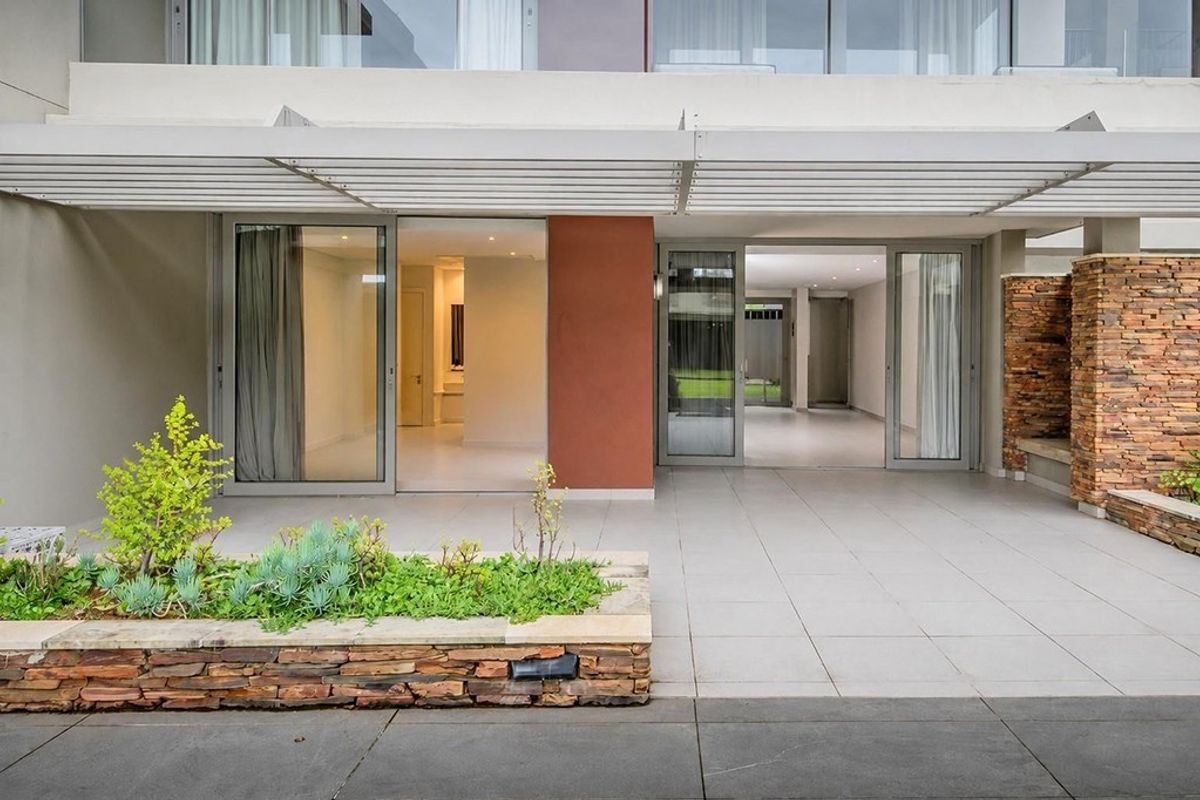 A modern covered patio featuring tiled flooring, a stone-clad planter box, and large sliding glass doors providing seamless access to the interior living space.