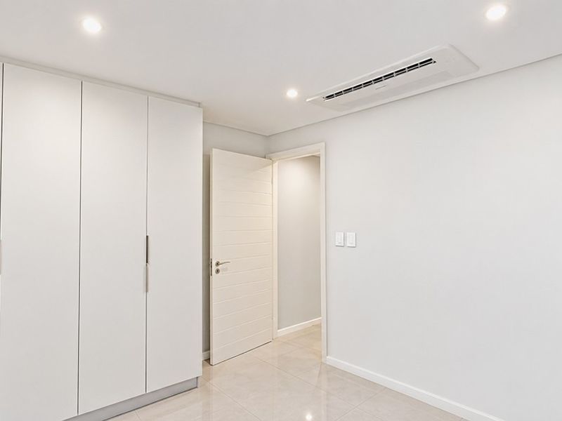 A bright, modern bedroom featuring sleek built-in cupboards, recessed lighting, ducted air conditioning, and neutral tiled flooring.