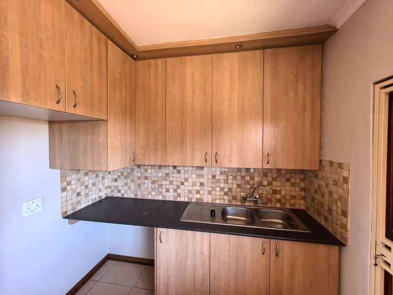 A functional kitchen area featuring light wood-look cabinetry, a mosaic tile backsplash, and a double bowl stainless steel sink with dark laminate countertops.