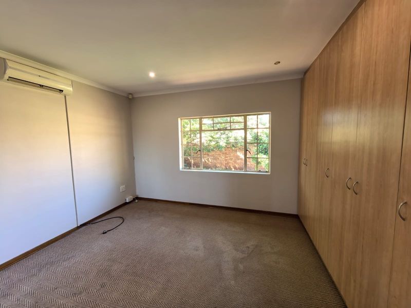 A spacious, empty bedroom featuring built-in wooden cupboards, carpeted flooring, and a wall-mounted split-system air conditioning unit.