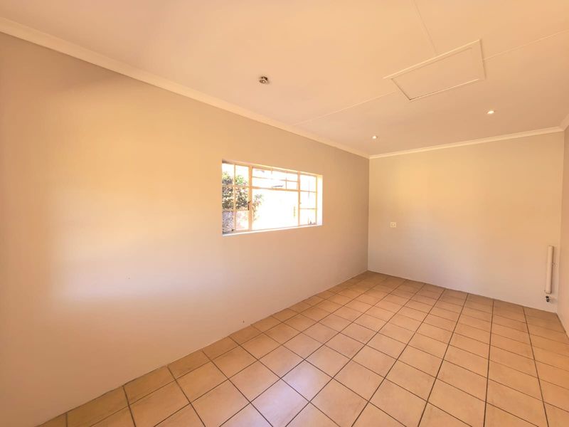 A bright, empty living area featuring neutral walls, tiled flooring, and a steel-framed window, providing a versatile blank canvas for interior design.