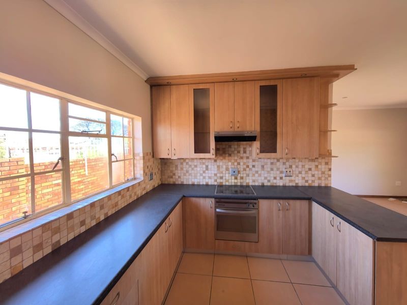 A functional kitchen featuring light wood-finish cabinetry, dark countertops, a mosaic tile backsplash, and integrated electric cooking appliances.