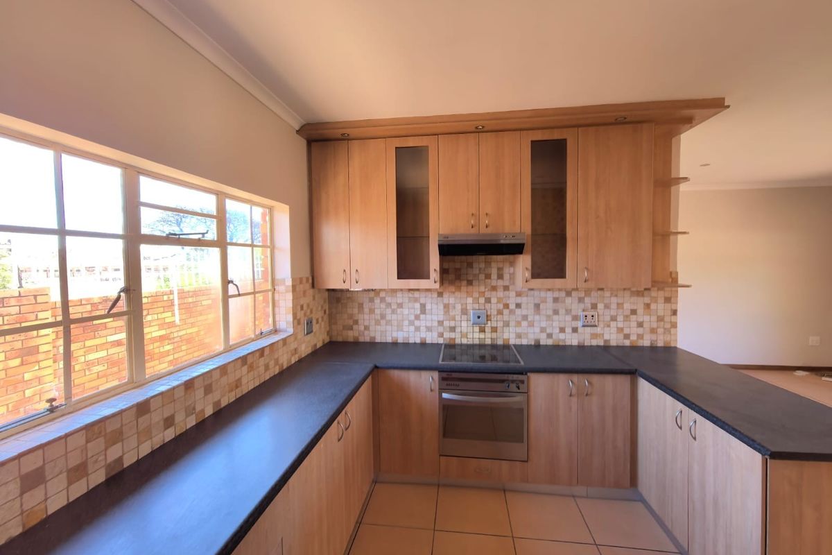 A functional kitchen featuring light wood-finish cabinetry, dark countertops, a mosaic tile backsplash, and integrated electric cooking appliances.