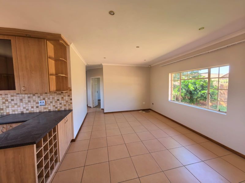 An open-plan living and kitchen area featuring tiled flooring, built-in wooden cabinetry with a wine rack, and large windows providing natural light.