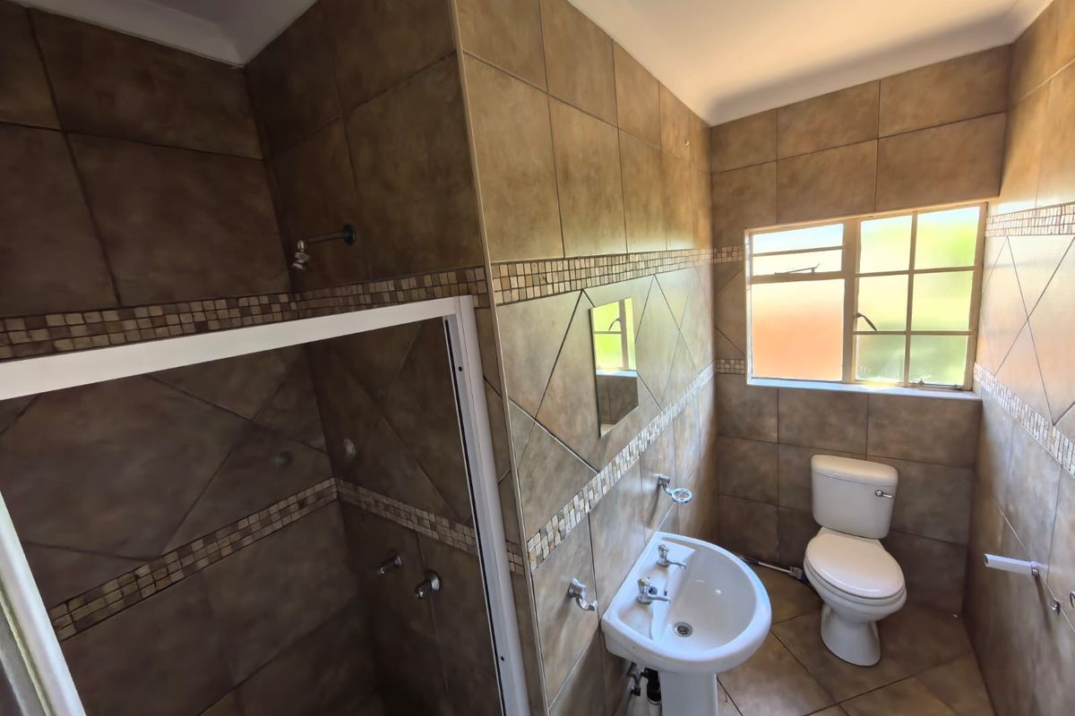 A functional bathroom featuring a pedestal basin, toilet, and a shower enclosure with full-height wall tiling and a window for natural light.