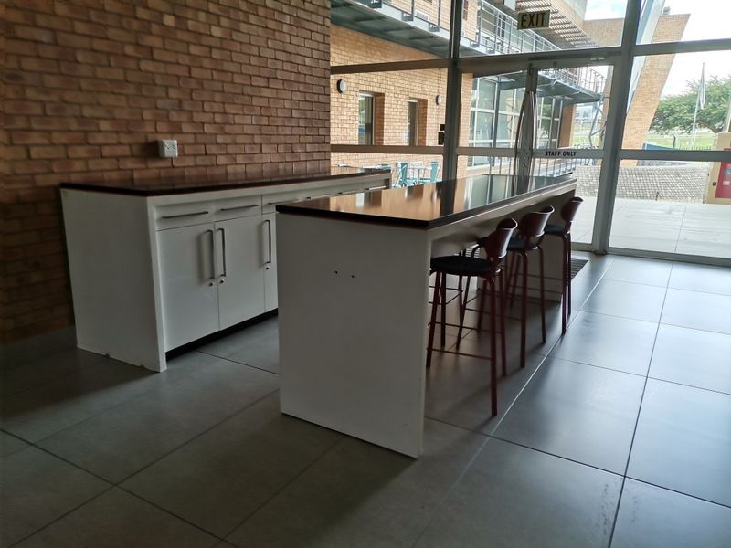 Modern commercial kitchenette area featuring built-in cabinetry, laminate countertops, and large format floor tiles, adjacent to a full-height glass entrance.