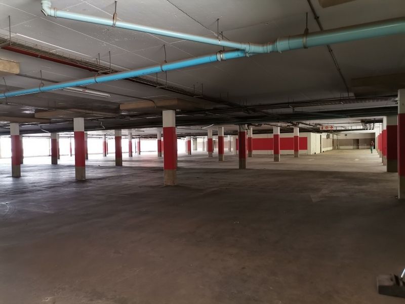 A large, open-plan commercial parking garage featuring exposed ceiling infrastructure, concrete flooring, and painted structural support columns.