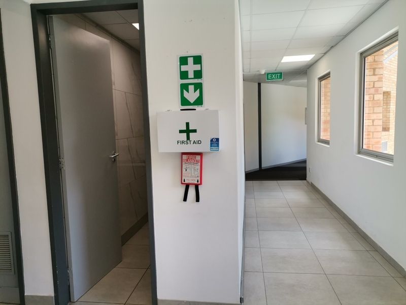 A clean, well-maintained commercial hallway featuring tiled flooring, recessed lighting, and wall-mounted safety equipment including a first aid station and fire blanket.