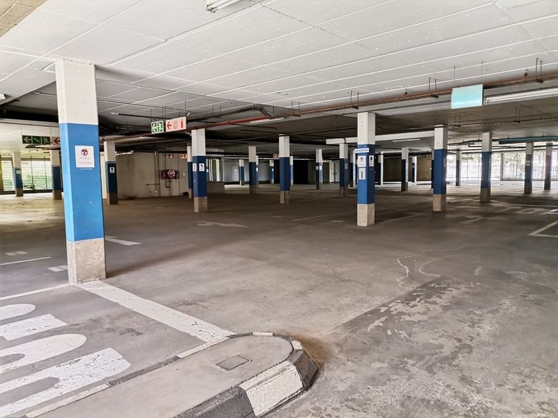 A spacious, open-plan commercial parking garage featuring concrete flooring, structural support columns, and clear directional signage.