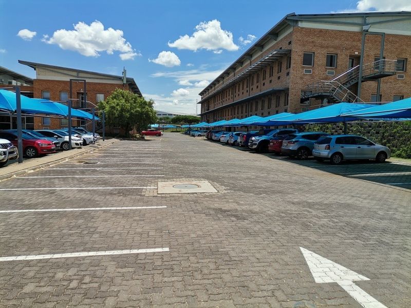 Commercial property exterior featuring a large paved parking area with shade cloth carports between two multi-story brick office buildings.