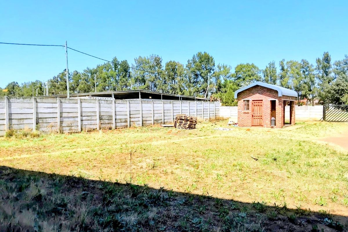 A spacious rear yard featuring a brick outbuilding, enclosed by precast concrete boundary walls and metal perimeter fencing.