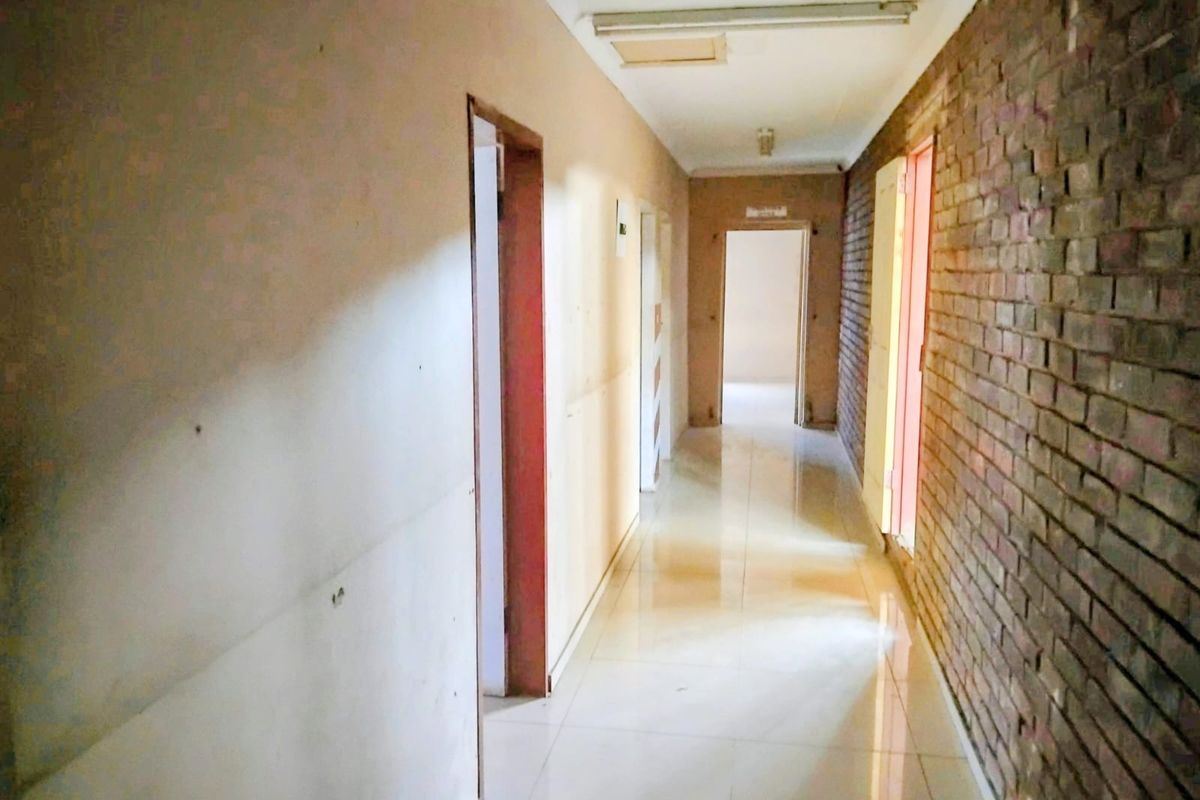 A long, empty commercial hallway featuring tiled flooring, exposed brickwork, and multiple doorways leading to adjacent rooms.