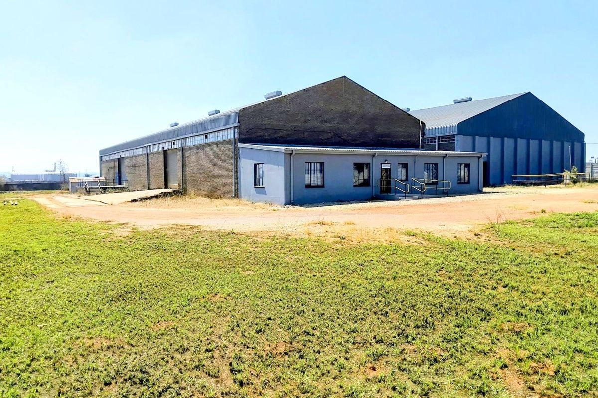 Commercial warehouse facility featuring a brick and metal exterior, loading ramp, and security-fitted windows, situated on a large open plot.