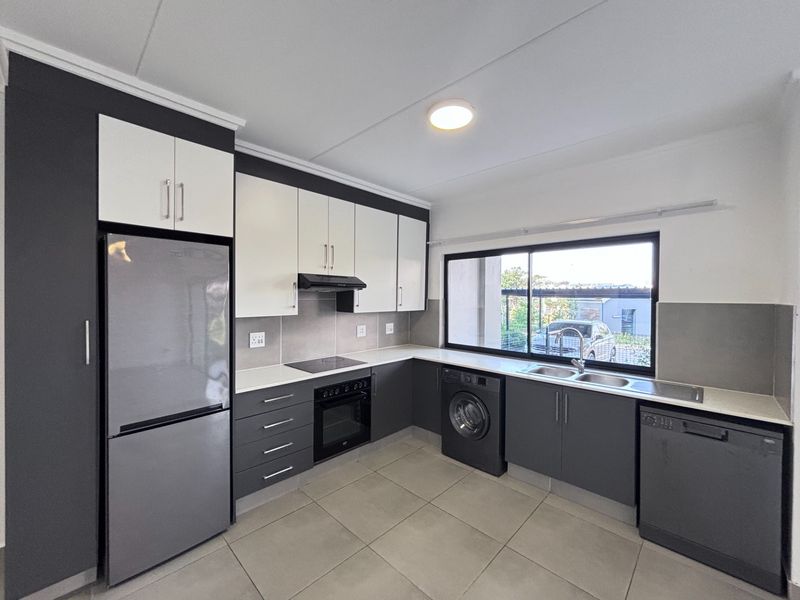 Modern kitchen featuring two-tone cabinetry, stone countertops, built-in oven, hob, extractor fan, and integrated plumbing for laundry and dishwasher appliances.
