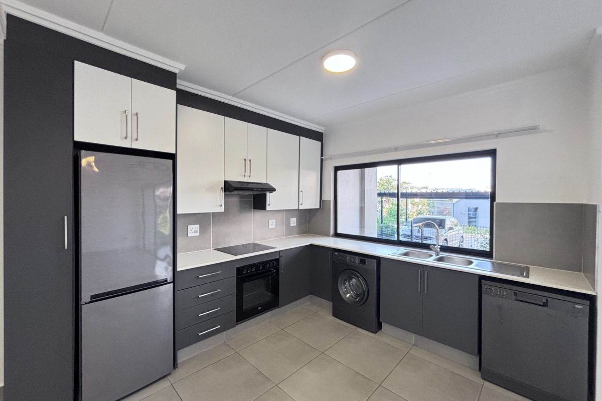 Modern kitchen featuring two-tone cabinetry, stone countertops, built-in oven, hob, extractor fan, and integrated plumbing for laundry and dishwasher appliances.