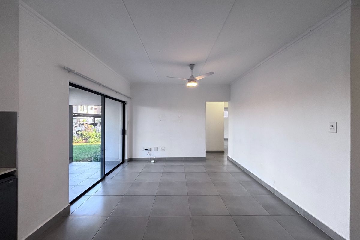 A spacious, empty living area featuring neutral tiled flooring, a ceiling fan, and a large sliding glass door providing access to the outdoor patio.