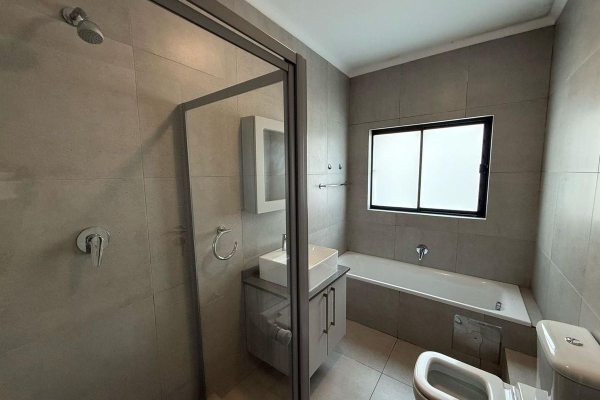 Modern bathroom featuring a glass-enclosed shower, a separate bathtub, a vanity with a vessel sink, and neutral floor-to-ceiling tiling.