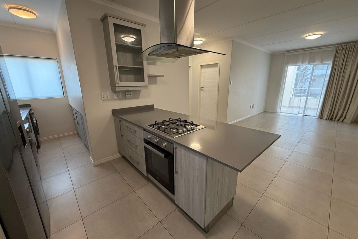 Modern open-plan kitchen and living area featuring a central island with gas hob, stone countertops, and direct access to a balcony.