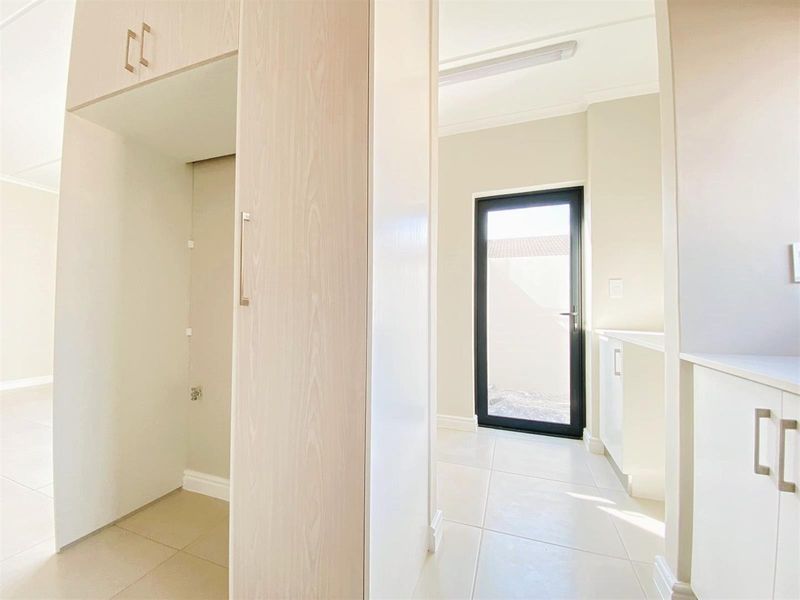 A clean, modern laundry area featuring built-in cabinetry, tiled flooring, and direct access to the exterior through a glass-paneled door.