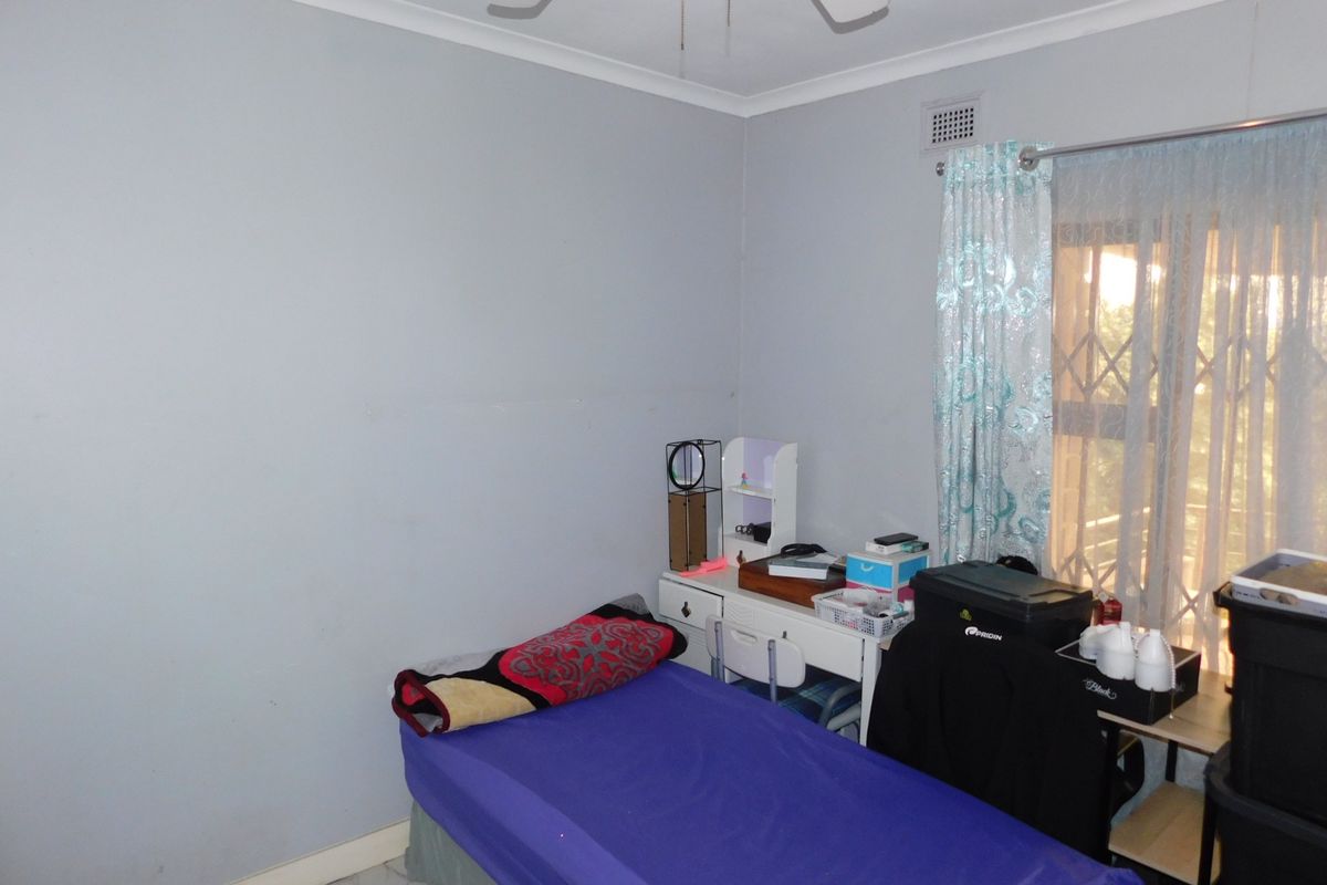 A standard bedroom featuring a ceiling fan, security gate on the window, and neutral wall finishes.