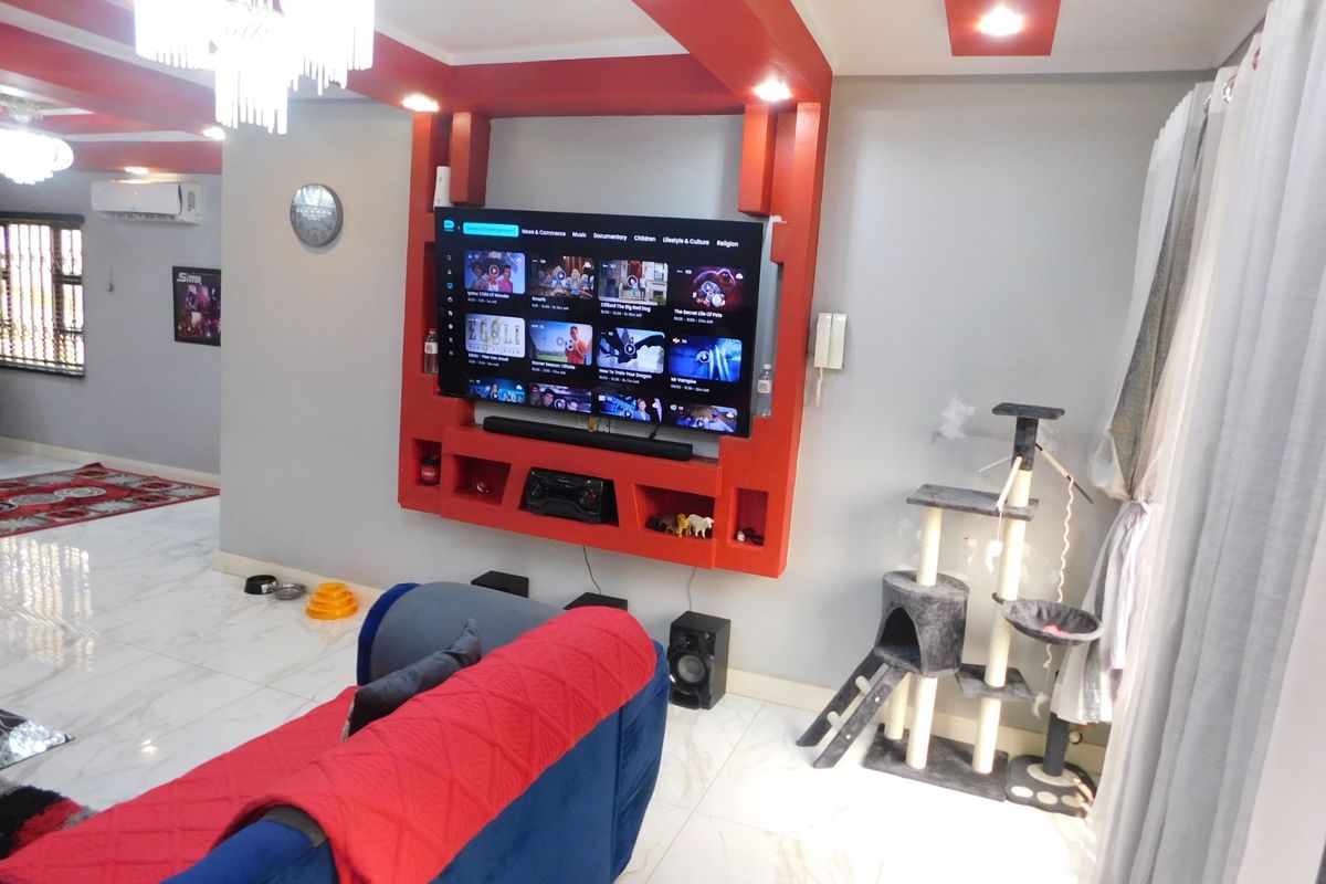 A modern living room featuring a custom red built-in media wall, recessed ceiling lighting, and polished marble-look floor tiles.