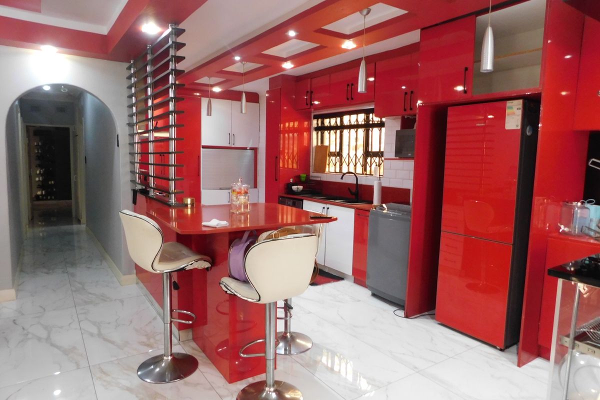 Modern kitchen featuring high-gloss red cabinetry, marble-look floor tiles, a breakfast bar, and recessed ceiling lighting, creating a bold and contemporary aesthetic.