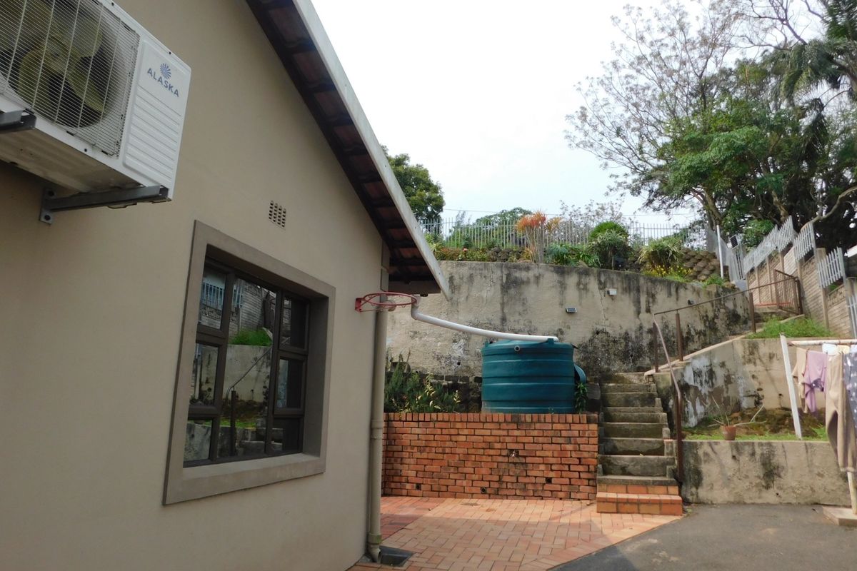 Rear exterior view showing a paved patio area, brick retaining wall, concrete stairs, and a water storage tank.