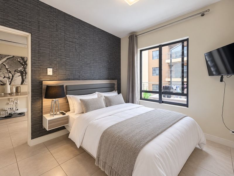 A well-maintained bedroom featuring a modern textured feature wall, tiled flooring, and large aluminium-framed windows allowing for natural light.