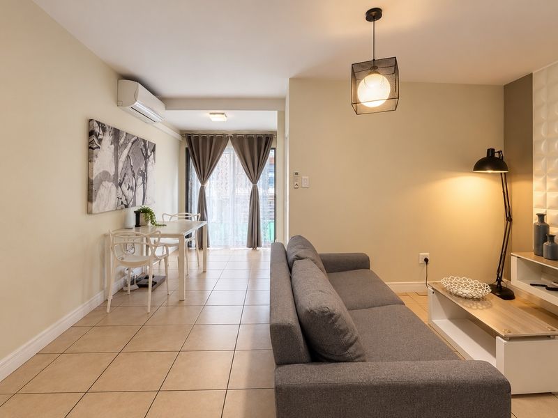 A well-maintained open-plan living and dining area featuring tiled flooring, a split-system air conditioner, and direct access to an outdoor space via sliding doors.